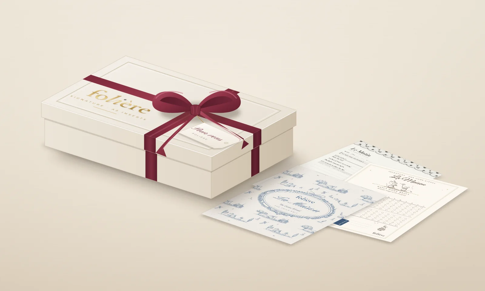 Packaging concept: an ivory box with a foil-stamped FOLIÈRE wordmark and a debossed frame, tied with a claret satin ribbon and a tag reading Pour vous, beside three inserts lying on the table