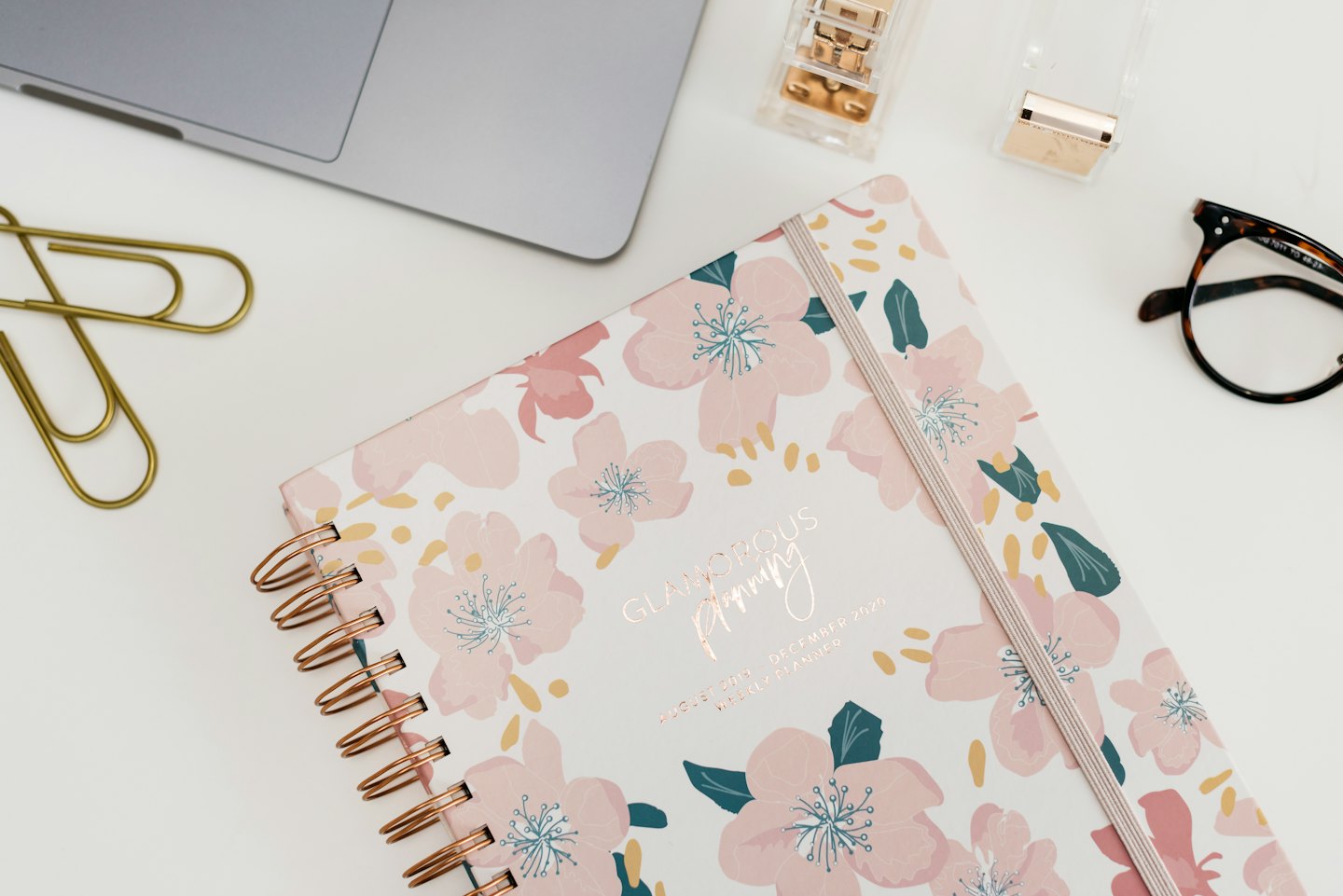 Floral planner and rose gold office supplies on a white desk.