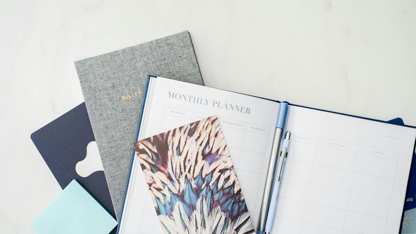 A monthly planner with pens and notebooks on a marble surface.