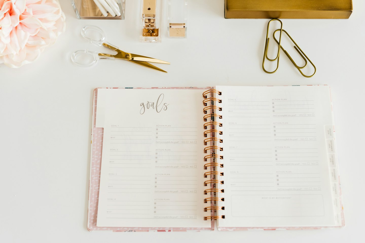 Open planner with goals and action plan on white desk with supplies.